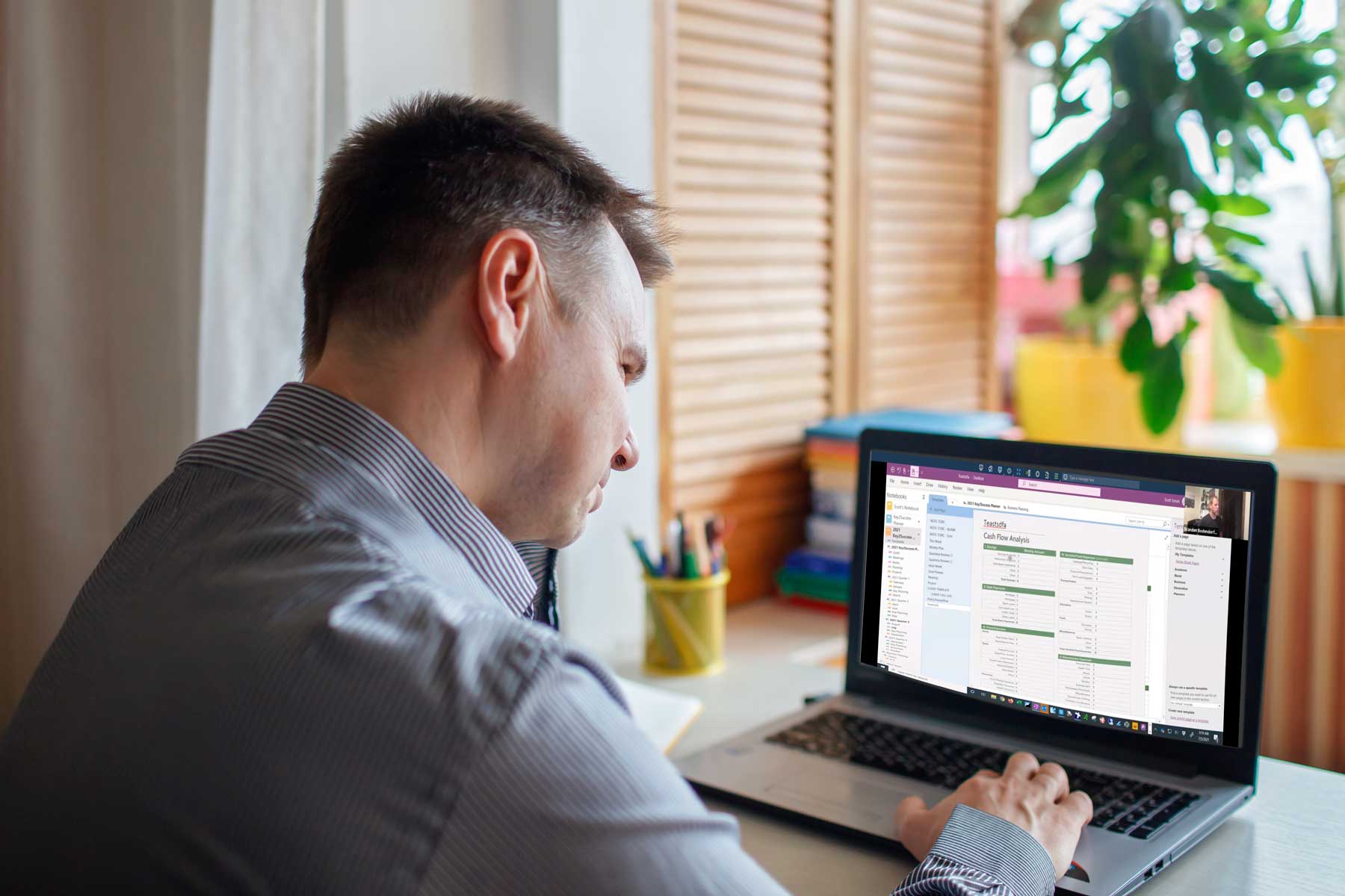 Man using a laptop to access OneNote for digital planning, surrounded by office supplies and a plant, representing personalized coaching sessions for effective digital organization.