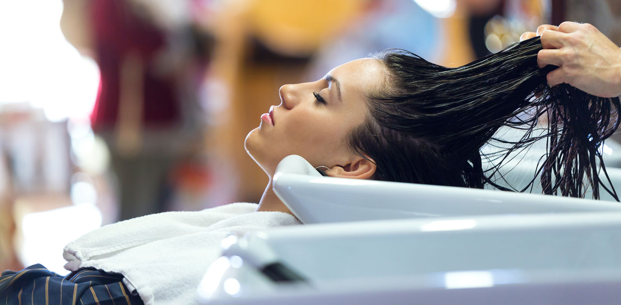 Woman relaxing in salon chair during hair washing, showcasing salon services and customer experience.