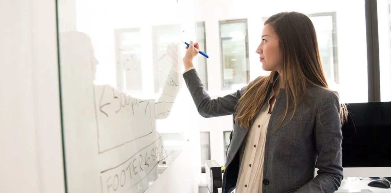 Woman in business attire writing on a glass board, illustrating ideas for client attraction strategies in a modern office setting.